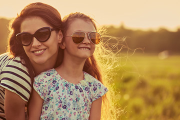 Happy fashion kid girl embracing her mother in trendy sunglasses in profile view and looking on...