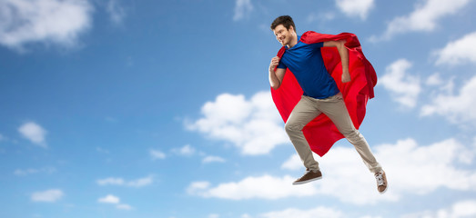 super power and people concept - happy young man in red superhero cape flying in air over blue sky and clouds background