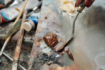 Woman artist draws a palette knife. Oil paints of different colors on the palette.