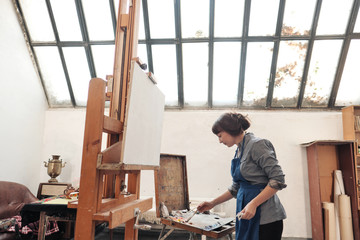 Young beautiful woman painter among easels and canvases in a bright studio.