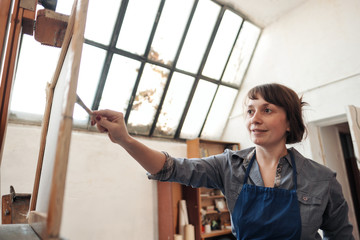 Young beautiful woman painter among easels and canvases in a bright studio.