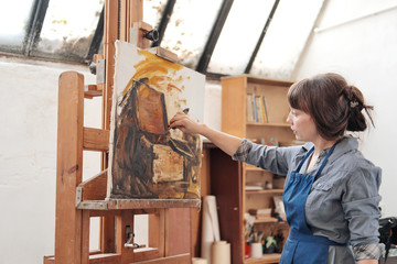 Fototapeta na wymiar Woman artist paints a picture on canvas. Bright art studio with a large window. Easels and canvases.