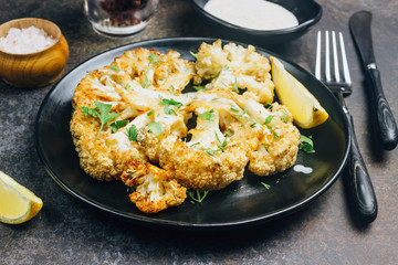 Fried cauliflower steak with greens and spices on dark background.