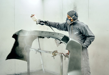 Un hombre pinta parte de la carrocería de un coche en un taller mecánico