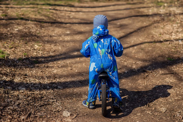 View from behind at a little toddler in a blue jumpsuit ready to kick off on his blue balance bike in spring on autumn park