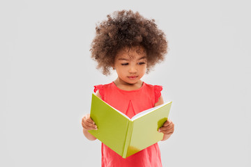 childhood, literature and people concept - sad little african american girl reading book over grey...