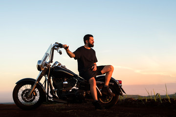 Plakat Young man sitting on his custom classic motorcycle admiring the landscape