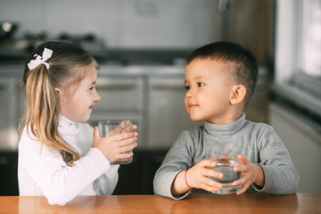 Children boy and girl in the kitchen holding glasses of water watching each other
