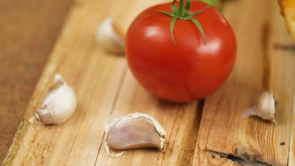 Fresh hot appetizing peperoni pizza lying on a wooden plate on the table decorated with basil greens, tomato and garlic in slow motion close up front view 4K video