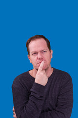 Man in deep thought finger on his lips looking up day dreaming on blue background