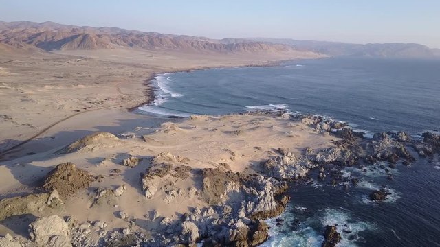 Las Tortolas beach aerial footage at Atacama Desert the sunset ray lights illuminate this amazing and idyllic beach in the middle of the desert, an arid awe landscape crashed by Pacific Ocean waters