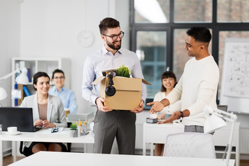 business, new job and corporate concept - male office worker with box of personal stuff and happy smiling colleague introducing workplace