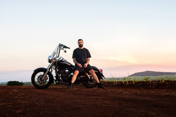 Young man sitting on his custom classic motorcycle admiring the landscape