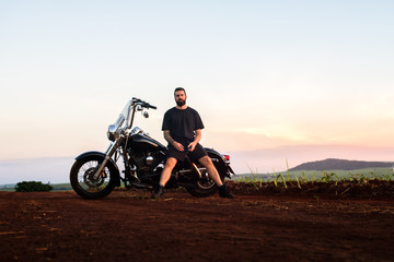 Obraz premium Young man sitting on his custom classic motorcycle admiring the landscape