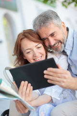 Happy mid adult couple taking a selfie on a tablet. Husband and wife using a tablet while sitting on a bench