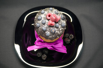 Easter cake with wild berries and chocolate icing with powdered sugar, decorated with purple ribbon