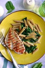 Whole wheat penne pasta with spinach and grilled chicken breast.Top view with copy space.