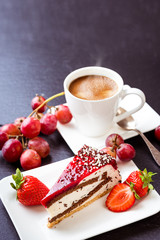 Dessert and coffee. A cup of hot coffee with crema, cake and fruit. Grapes, strawberries and fruit cake. Still life on a dark background