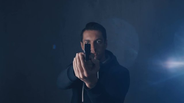 Portrait of dangerous mercenary or assassin is aiming a pistol against a dark background.