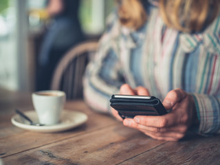 Young woman drinking coffee and using smartphone