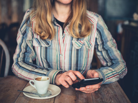 Young woman drinking coffee and using smartphone