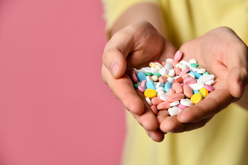 A handsome man in T-shirt on a pink background holding pills in his hand