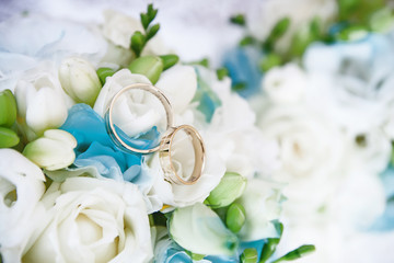 Two golden wedding rings on white and green flowers bouquet.