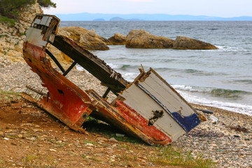 An abandoned old, ruined boat wreck on the shore. Back View. Grass in front and the sea at back.