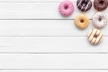 Glazed decorated donuts for sweet break on white wooden background flat lay copy space