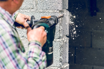 Construction industry worker using pneumatic hammer drill to cut the wall concrete brick, close up