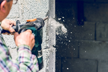 Construction industry worker using pneumatic hammer drill to cut the wall concrete brick, close up