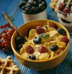 Healthy breakfast with corn flakes, berries, waffle and milk on blue background