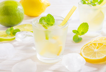 Two glasses with summer drink mojito with lime, lemon and mint, with ice cubes on white wooden background.