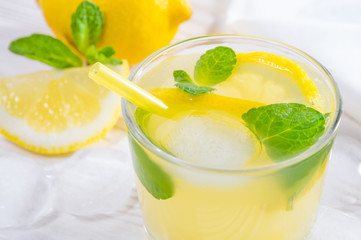 Summer drink of lemon and mint, or lemonade, with ice cubes on white wooden table.