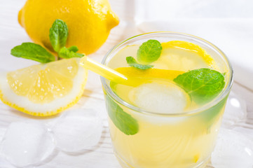Summer drink of lemon and mint, or lemonade, with ice cubes on white wooden table.