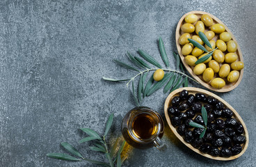 Glass bottle of homemade olive oil and olive tree branch, raw turkish green and black olive seeds and leaves on grey rustic table. olives background, olivae oleum