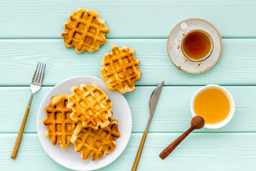 Traditional belgian waffles with honey and tea on served mint green wooden table background top view