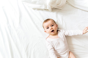 Happy and smiling adorable 6 month old baby girl lying on a bed, lifestyle isolated on natural white background.