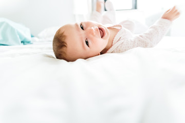 Fototapeta na wymiar Happy and smiling adorable 6 month old baby girl lying on a bed, lifestyle isolated on natural white background.