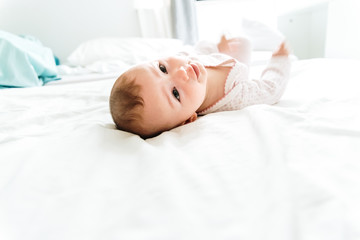 Happy and smiling adorable 6 month old baby girl lying on a bed, lifestyle isolated on natural white background.