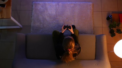 Closeup top shoot of pretty female playing video games while sitting on the couch indoors in a cozy apartment with lights off