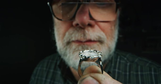 Slow motion of experienced goldsmith controlling a quality of just finished handmade jewelry ring with precious diamond stones. Shot in 8K. Concept of jewelry, luxury, goldsmith, diamonds, brilliance.