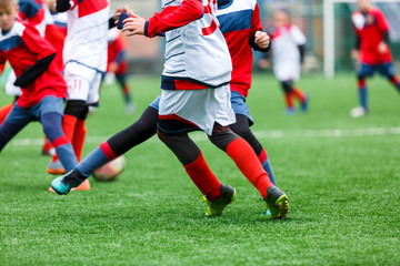 Boys kick soccer ball. Footballers run after the ball on green grass. Kids in white and red shirts dribbling, improve skills. Training, football, hobby, active lifestyle