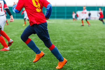 Obraz premium Boys kick soccer ball. Footballers run after the ball on green grass. Kids in white and red shirts dribbling, improve skills. Training, football, hobby, active lifestyle