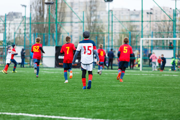 Obraz premium Boys kick soccer ball. Footballers run after the ball on green grass. Kids in white and red shirts dribbling, improve skills. Training, football, hobby, active lifestyle
