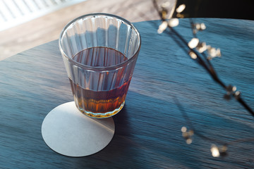 Transparent glass with tea and beer coaster on wooden table. 3d rendering.