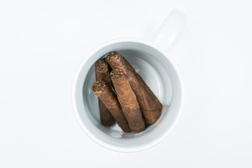 Brown cigars from twisted sheets in mug with white background.
