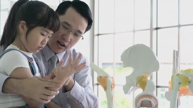 Little girl learning about human structure and skeleton model with asian doctor in modern laboratory of hospital. Concept of science, education, muscle healthy and anatomy bone.