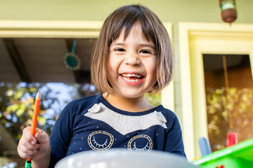 Portrait of a preschool aged girl holding a colored pencil and smiling.