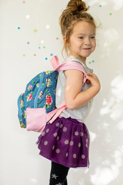 Portrait of a preschool aged girl wearing a back pack in front of a white back drop.